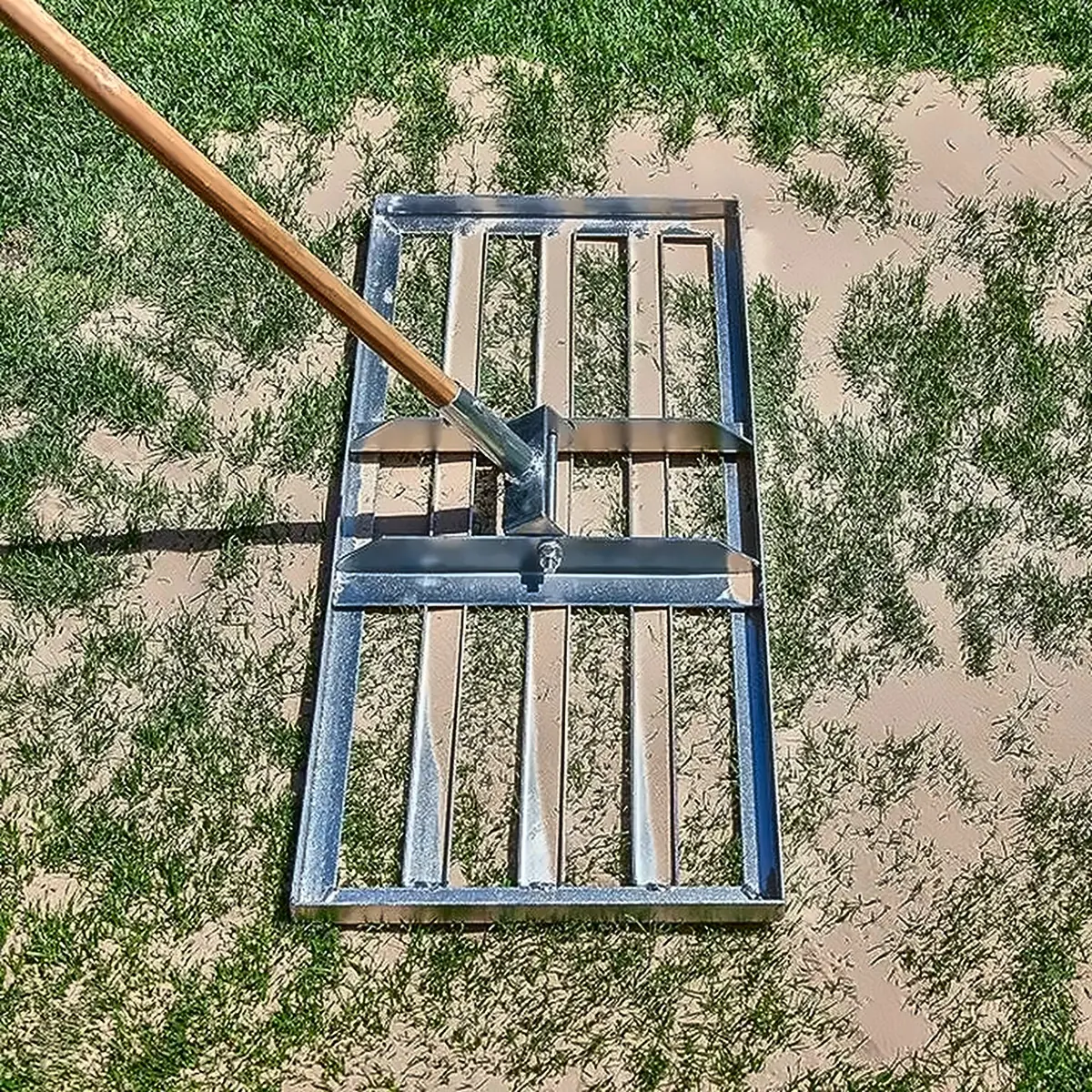 Levelling rake spreading top dressing across new turf